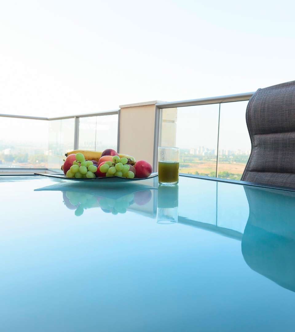 This image is of a glass-top table outside on a balcony with fruit and a drink on it. Pane Free Glass in Manchester, NH uses tempered glass, resistant to scuffs and cracks as well as the elements, so your table will stay looking new for longer.
